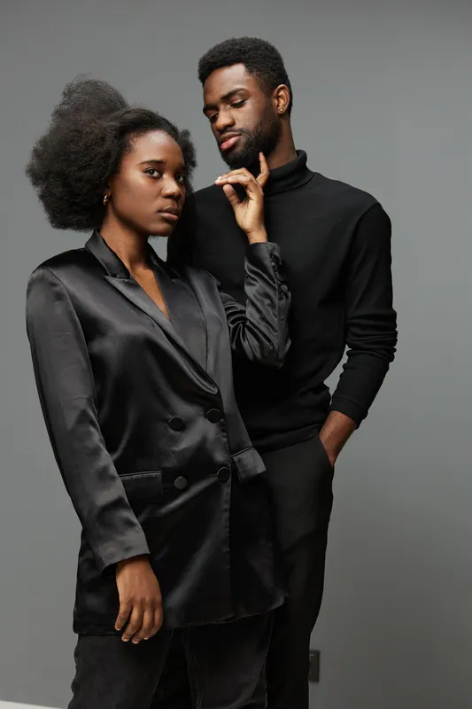 Stylish African couple in black attire showing confidence against a minimalist gray background, embodying modern elegance and intimacy