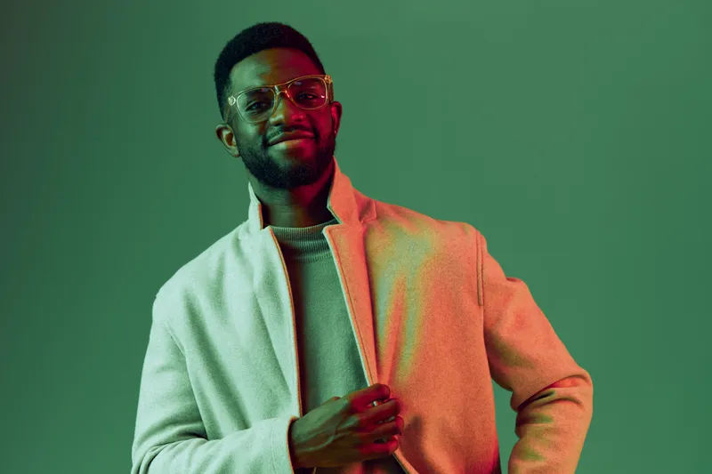 A stylish African American man exuding confidence in a light coat against a vibrant green backdrop, showcasing modern fashion, emotions, and individuality