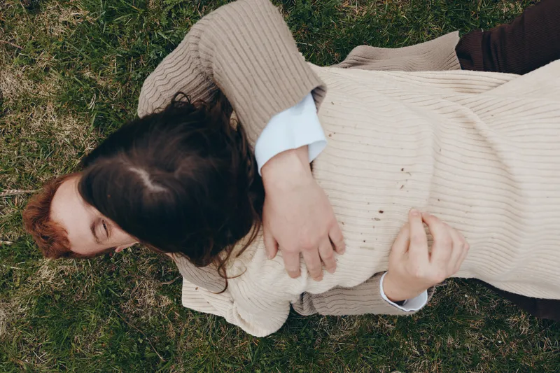 Lifestyle moment outdoors with a person resting on grass in a sweater, soft light and natural colors, relaxed posture, intimate mood, candid scene, comfort, moment, nature, calm, serenity, warmth,