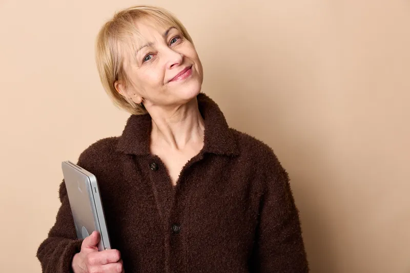 elderly woman smiling holding smartphone, studio portrait on beige background, soft light, focused on technology communication, daily life, modern connection