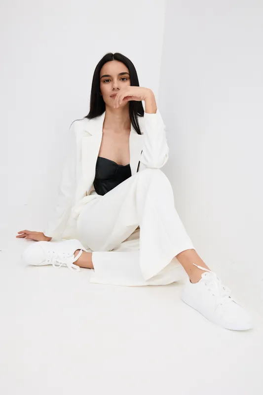 stylish woman in white suit sitting on floor against white background, black top and white sneakers, relaxed pose, minimalistic studio setting