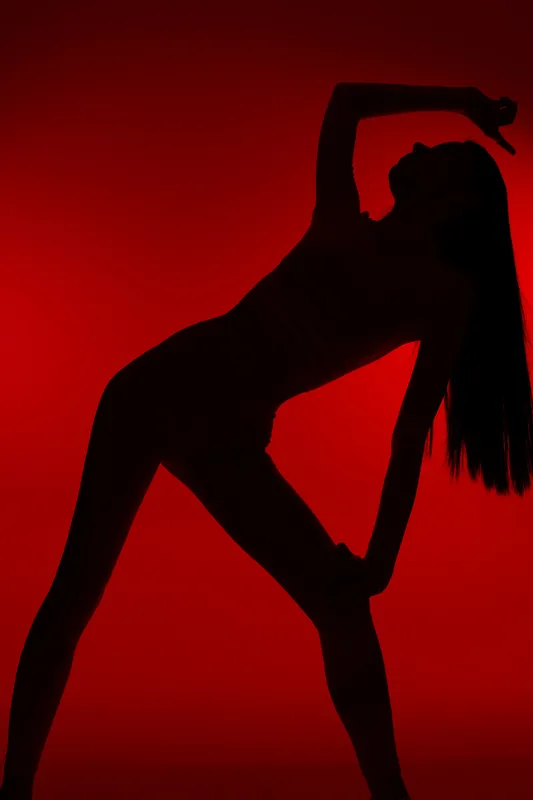 Woman sport fitness silhouette in dynamic stretching pose against vibrant red background, showcasing strength, flexibility, and athletic lifestyle in artistic lighting.
