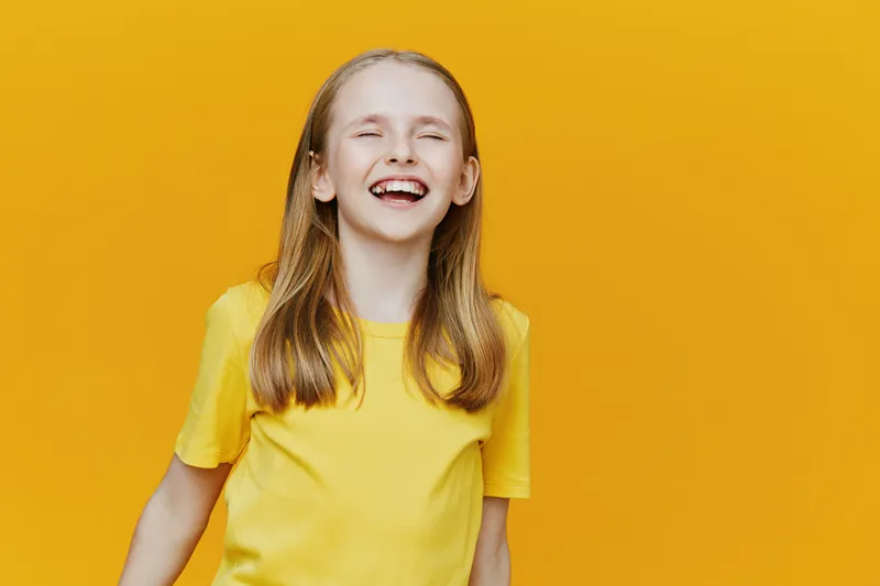 Happy young girl with long hair smiling against a bright yellow background, wearing a yellow t shirt, embodying youthful joy and positivity