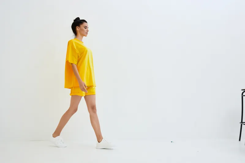 young woman walking confidently in bright yellow casual outfit and white sneakers against plain white background, modern minimal style