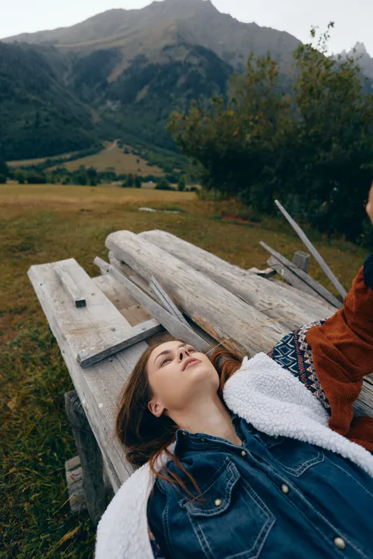 woman portrait nature mountain meadow bench relax outdoor lying on wooden plank in alpine field, casual fashion jacket and cozy blanket, peaceful travel moment and scenic landscape