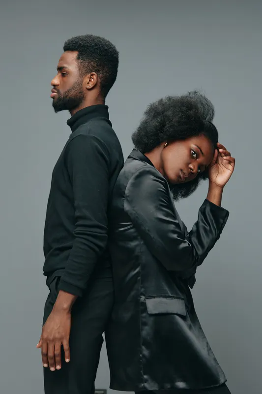 A stylish African couple posing back to back, showcasing modern fashion and strong emotions, with a minimalistic gray background for a contemporary look