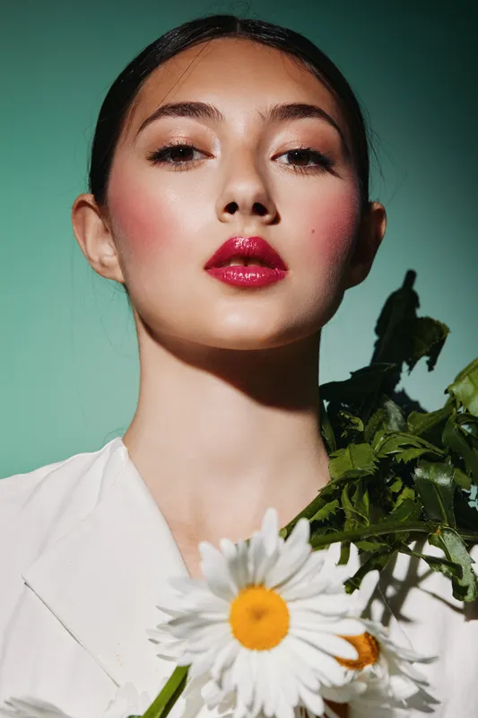 Portrait of a stylish young woman with bright red lipstick holding fresh white daisies wearing white fashion outfit, studio beauty concept with creative natural makeup look.