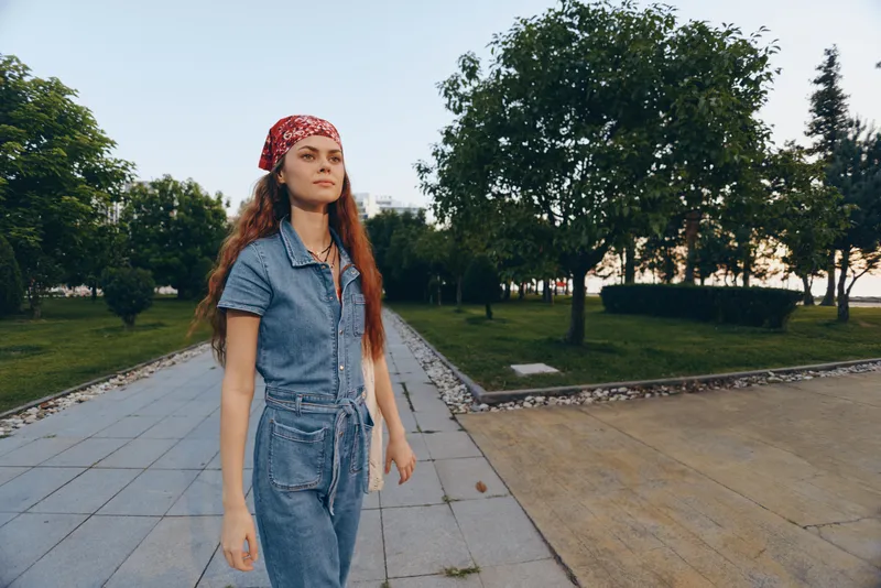 Lifestyle woman in modern boho-western denim street style walks confidently outdoors with film color tones enhancing her casual summer look and natural surroundings.