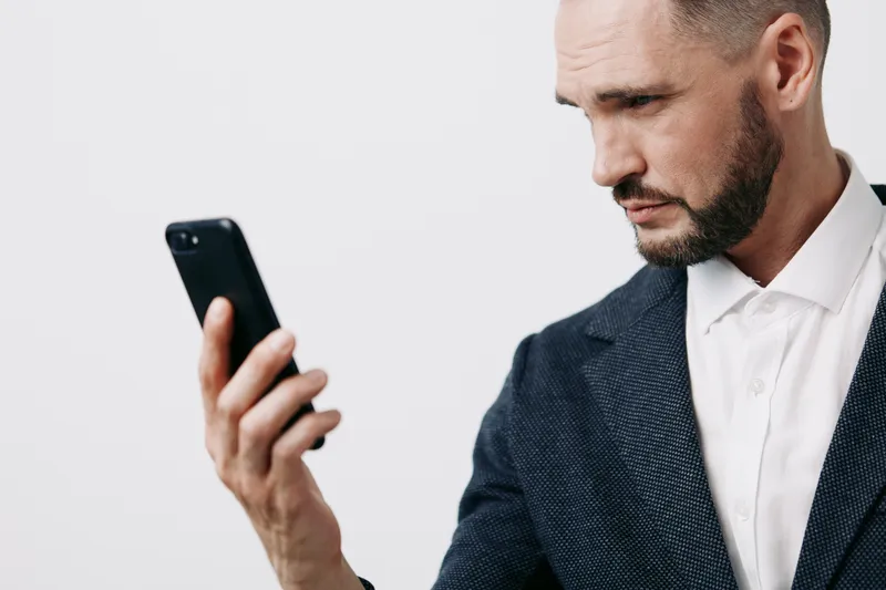 A professional man in a business suit reviews a smartphone against an isolated colored backdrop, conveying focused mindset, confident mood, and determined attention.