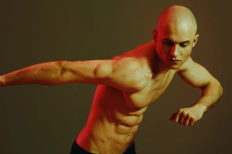 Athletic man performing a dynamic pose, showcasing strength and confidence in a vibrant low-light setting. Unique lighting enhances the image's dramatic effect.