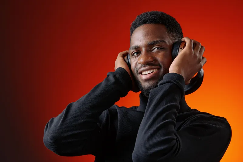 Young African man enjoying music with headphones against a vibrant orange background, expressing joy and relaxation, perfect for promoting audio experiences