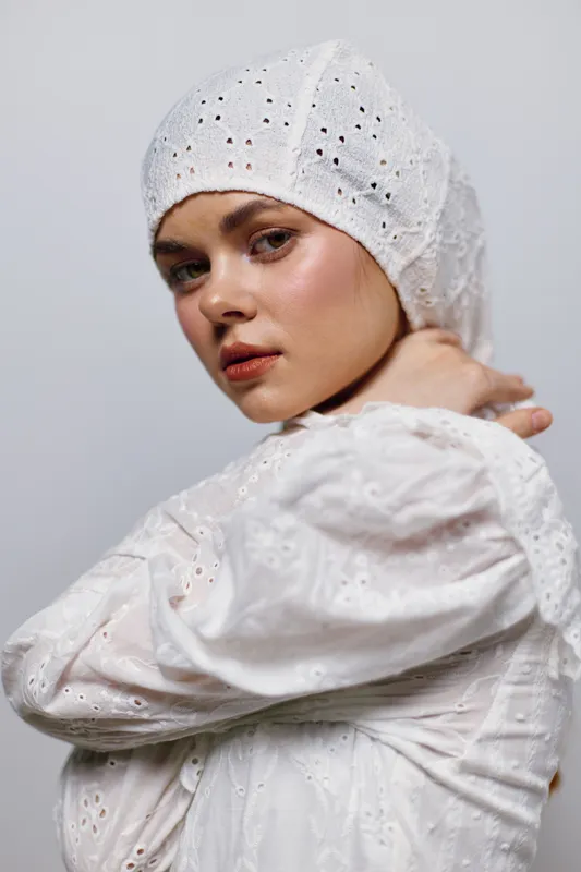 Elegant young woman in a white vintage dress and headscarf, expressing confidence and grace with a soft background