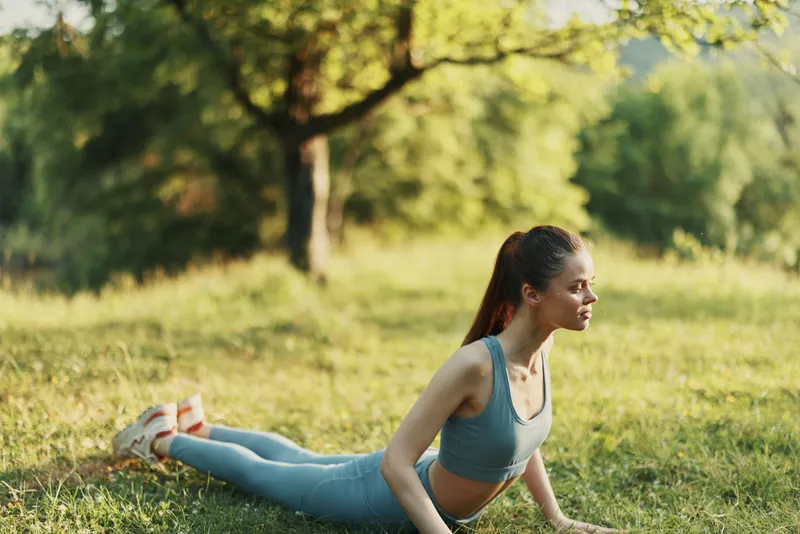 Young woman practicing yoga outdoors in a serene nature setting, in sporty attire, showcasing strength and balance, embodying healthy lifestyle and mindfulness