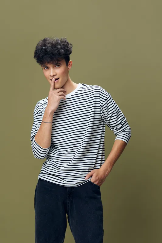 young man in striped shirt posing thoughtfully with finger near lips against olive background, casual style, curly hair, studio portrait