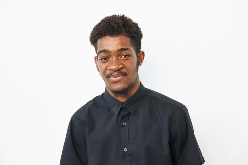 Young African American man with a warm smile, wearing a black shirt, against a white background. A playful and joyful expression highlights his personality.