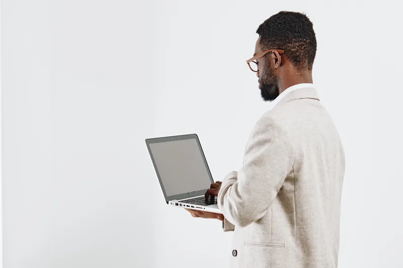 Professional confident young African American man in smart casual clothing using laptop computer in studio setting. Business, technology, workplace, communication, modern, professional concept.
