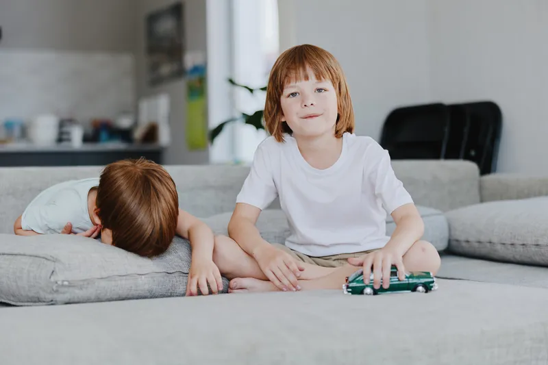 Playful boys enjoying time at home, one with a toy car and the other resting. Bright living room setting creates a cheerful atmosphere.