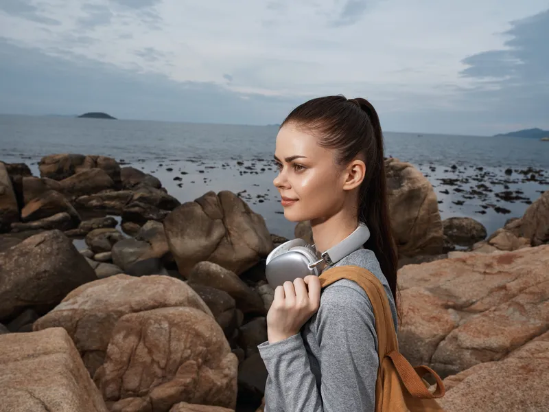 Young woman in activewear with headphones by the seaside, showcasing a calm expression against a rocky background, perfect for wellness and outdoor lifestyle concepts