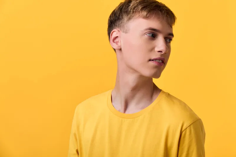Young male in a yellow tshirt against a yellow background creates a bright minimal fashion lifestyle shot with clean lighting and strong color harmony and contemporary vibe