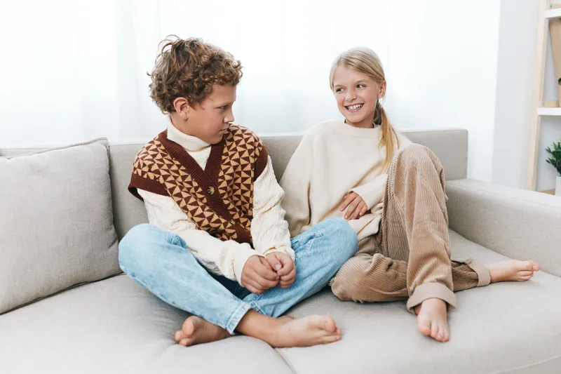 An authentic lifestyle scene featuring children at home with a cozy mood, a school inspired vibe, and playful interaction on a sofa.