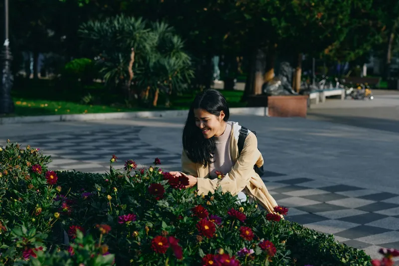 Woman tending vibrant flowers in a park, close attention to blossoms and greenery, soft sunlight, serene outdoor setting, casual attire, focused activity, calm mood, This candid scene captures