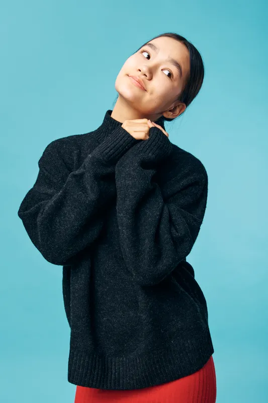Young woman wearing black sweater and red skirt posing thoughtful on blue background. Fashion portrait with casual clothing, studio light and serene expression indoors for lifestyle concept.