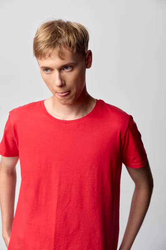 Man wearing red t shirt in casual pose, looking to the side, studio lighting, simple background, fashion style, everyday apparel, natural expression, relaxed mood, clean composition