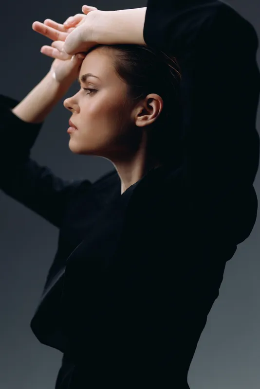 young woman posing with arms raised wearing black clothing against dark background