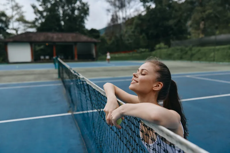 A young athlete enjoying a moment of relaxation on a tennis court, showcasing joy and confidence in a vibrant outdoor setting, perfect for sports photography
