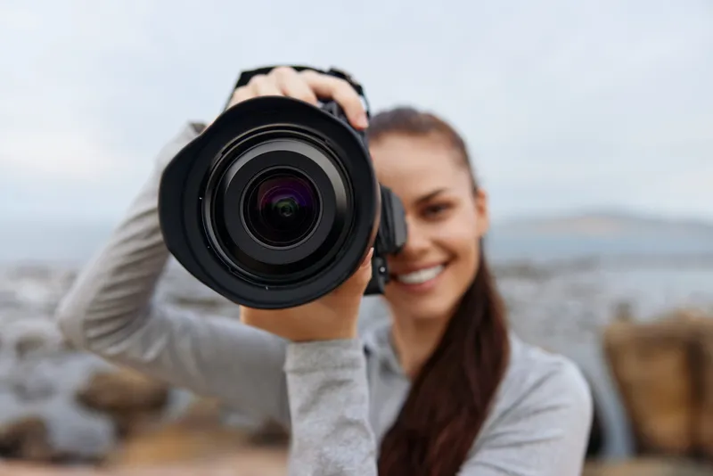 Smiling female photographer taking pictures outdoors with a professional camera, showcasing passion for photography in a natural setting