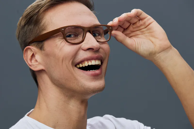 Close-up of smiling happy young caucasian man wearing glasses looking at camera holding in hand, casual style, joyful expression, studio portrait, gray background, lifestyle concept, cheerful mood, po
