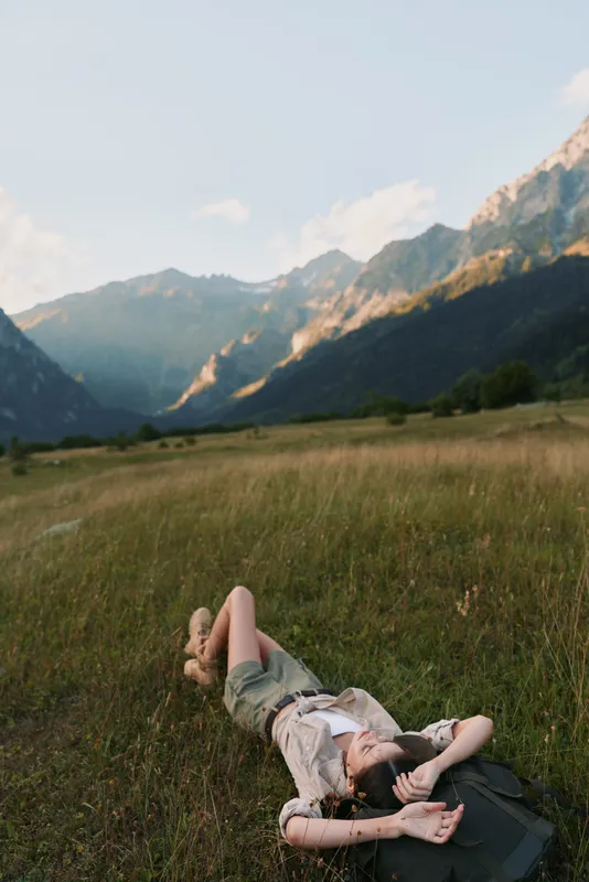 Woman lifestyle outdoor relaxation nature mountains meadow sunlight carefree scenery, casual clothing, serene moment, bright colors in a natural setting