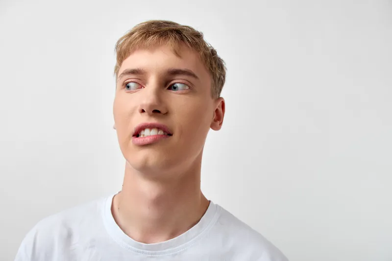 Young man in a white t shirt with a curious expression turning to the side, casual style, clean studio backdrop, relaxed mood, thoughtful glance, everyday portrait vibe