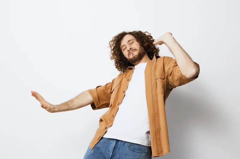 Joyful young man dancing in a casual outfit against a minimalistic background, expressing happiness and freedom through movement and style