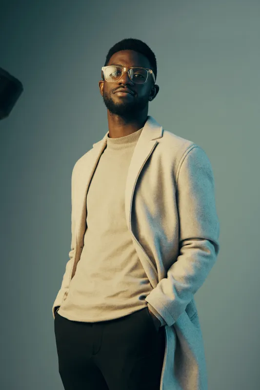 Stylish African man in elegant coat smiles confidently against a soft blue background, showcasing modern fashion and sophistication in urban style