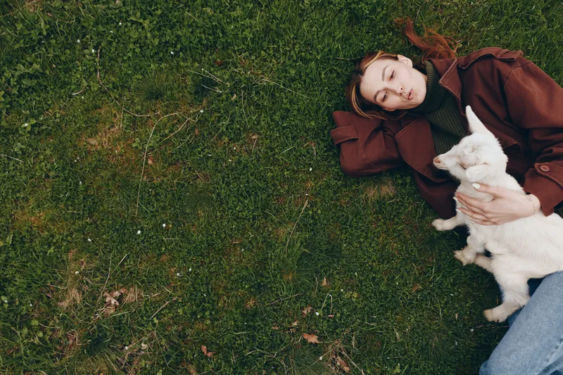 woman outdoors dog grass relaxation casual lifestyle nature friend pet in a sunlit moment, the woman lies on green grass, smiling gently, embracing a small dog, showcasing candid comfort and outdoor