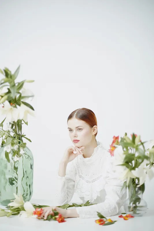 Elegant woman surrounded by flowers in a soft white setting, conveying tranquility and beauty through delicate colors and thoughtful expressions
