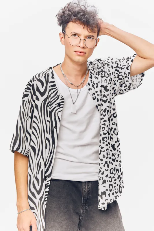 Young man wearing round glasses and a stylish animal print shirt, posing confidently against a white background with a casual and modern look.