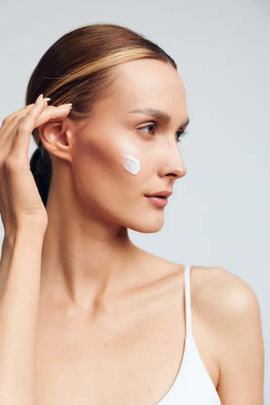 Young woman applies moisturizer cream on her face with fingers closeup natural skincare routine healthy skin isolated on white background beauty care concept