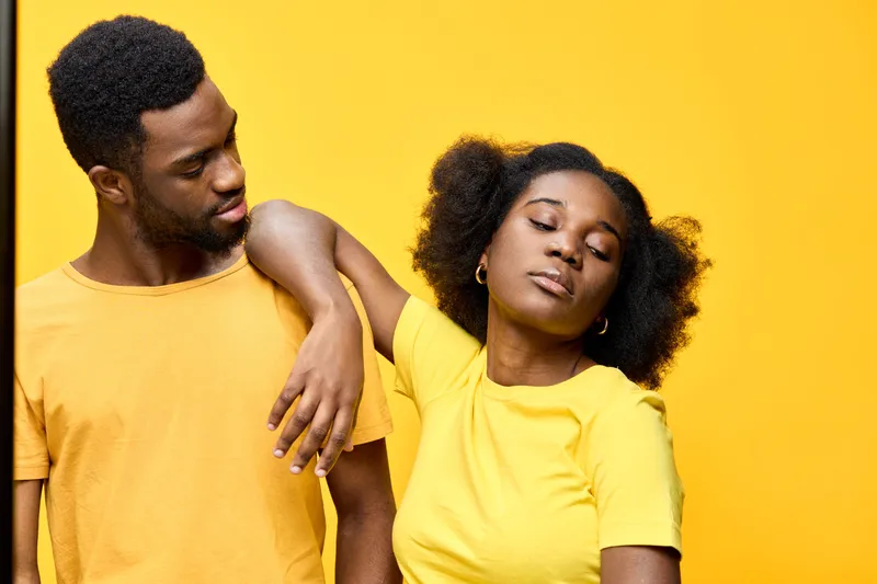 Young African couple in matching yellow outfits against a bright yellow background, expressing love and joy through their playful interaction and emotions