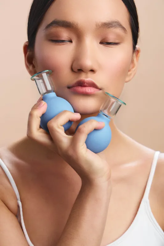 asian woman with closed eyes holds two small blue dumbbells near her face in a clean studio, creating a calm wellness moment that highlights self care, balance, and gentle strength.