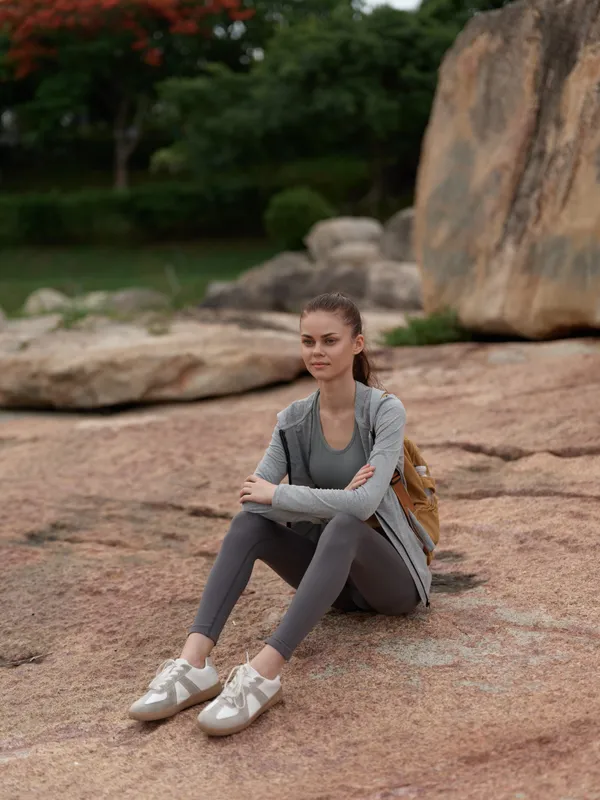 Young woman in activewear sitting on rocky terrain, displaying a pensive expression, perfect for fitness and outdoor themes