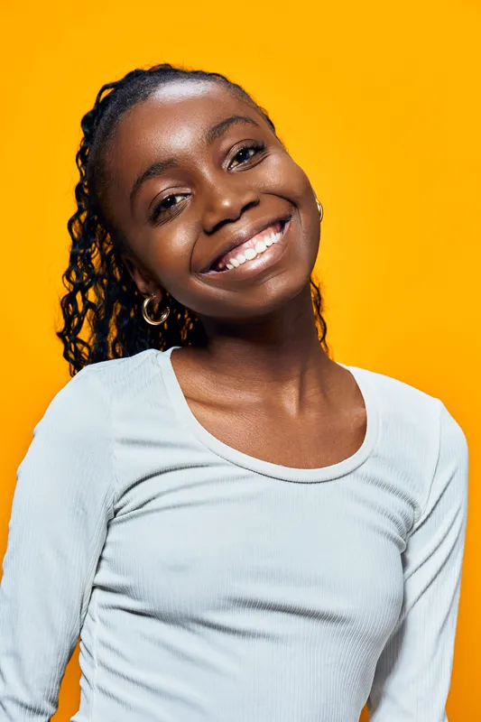 Happy young girl with curly hair smiling against a vibrant yellow background, showcasing joy and confidence, ideal for themes of positivity and youth