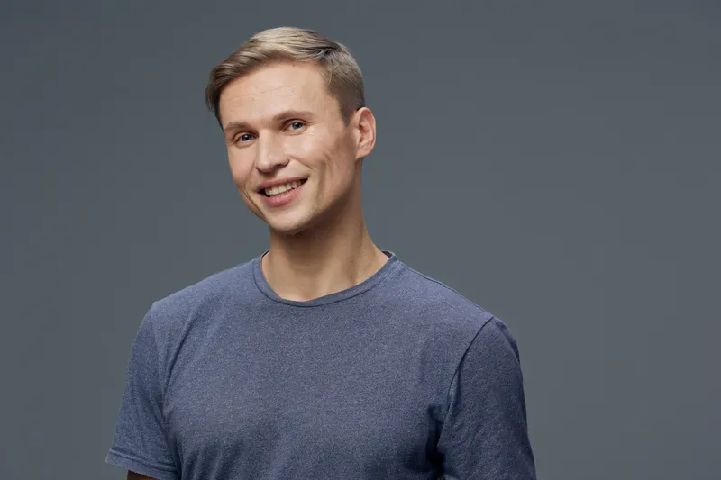 Smiling man with short light brown hair wearing casual blue t-shirt looking at camera isolated on gray background studio portrait. People lifestyle concept, positive expression, comfortable style, cas