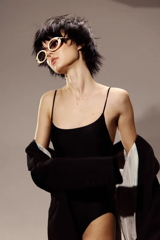 stylish woman wearing black bodysuit and oversized sunglasses with short hair and confident pose