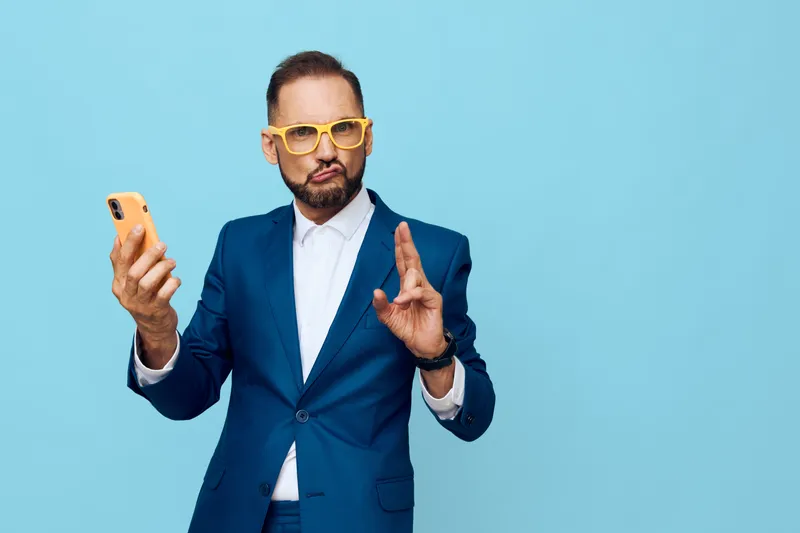 A professional man in a blue suit on a solid blue background, expressing confidence and focus while using a smartphone in a moment of business communication.