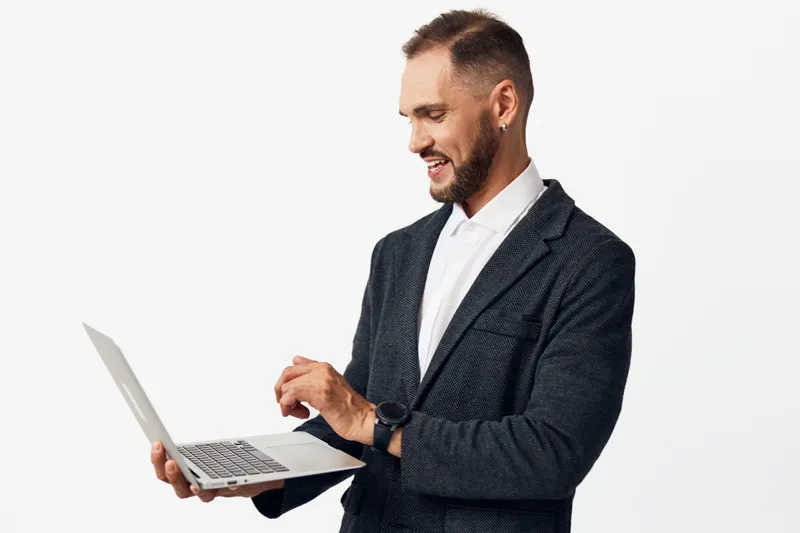 Businessman in a dark blazer works on a laptop, focused and confident against a clean colored background. He conveys professionalism, motivation, and optimism as he engages with technology in a