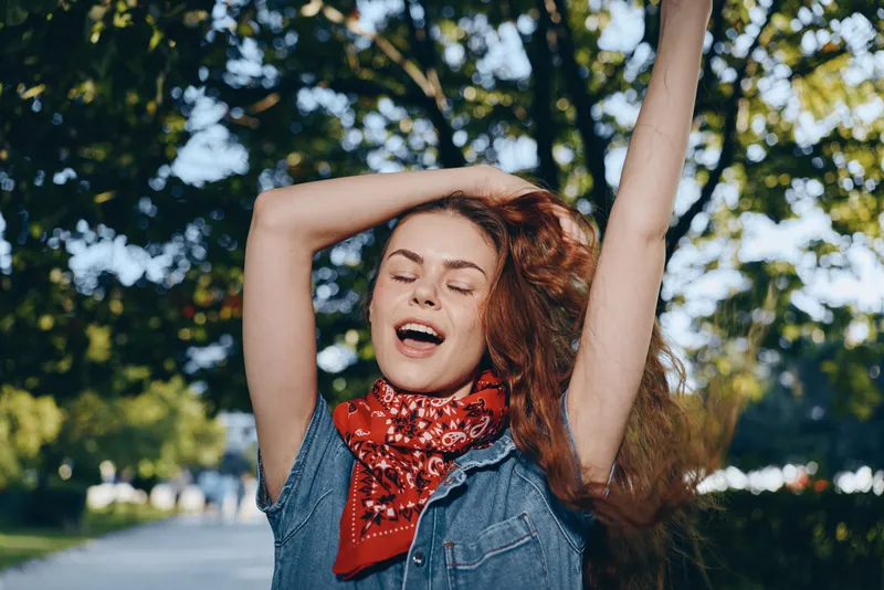 Lifestyle woman enjoying outdoor moment in modern boho-western denim street style with red bandana and film color tone, expressing freedom and joy in natural light.