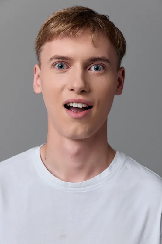 Surprised man with wide eyes and open mouth wearing a white tshirt, conveying astonishment and curiosity in a clean studio setting, ideal for expressive media project needs