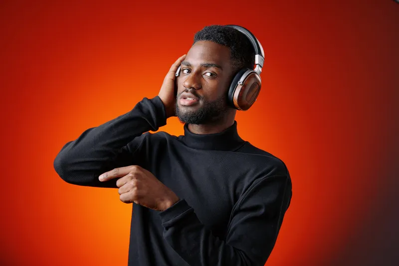 Young African man in black turtleneck posing with headphones, expressing joy while pointing, against an orange background representing music enjoyment